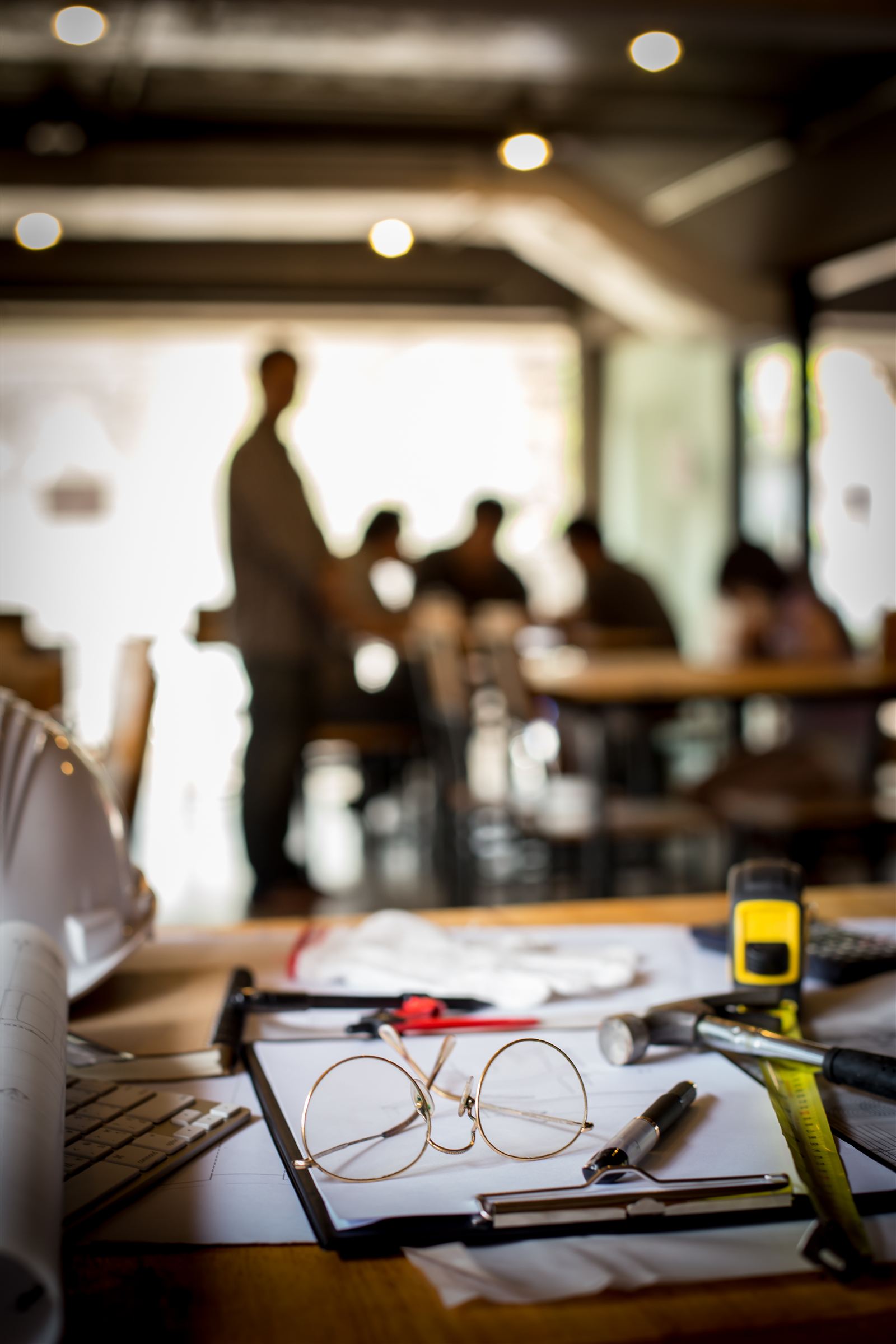 Paperwork and reading glasses on a desk in a busy workplace
