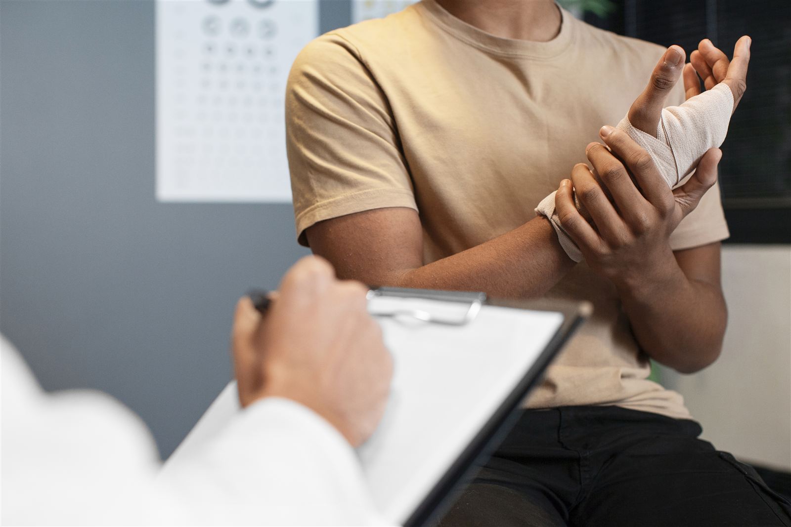 Doctor taking notes beside a patient with a bandaged wrist
