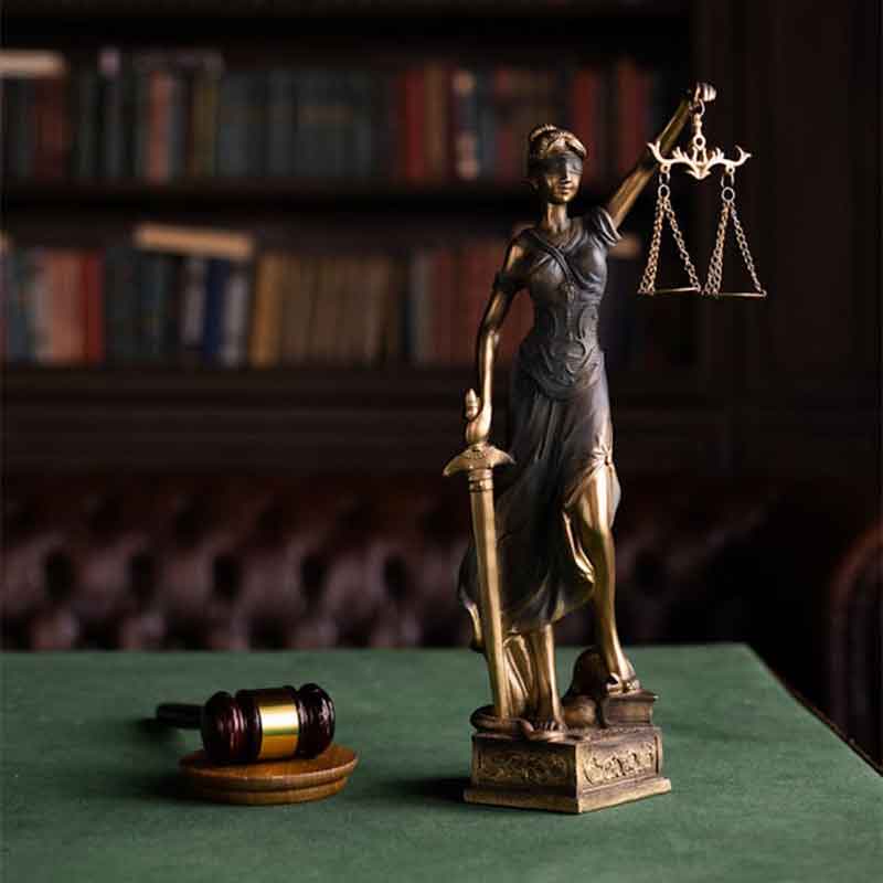 Statue of Lady Justice and a gavel on a desk in front of bookshelves